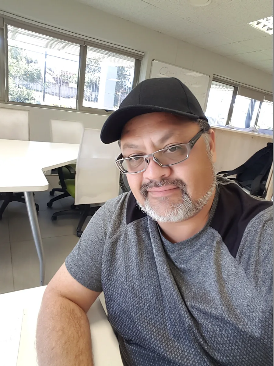 Portrait of the artist Gershwynn Kay, smiling, wearing a black cap and glasses.